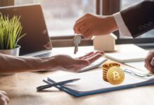 Real estate agent handing keys to home buyer with stack of Bitcoin on the table.
