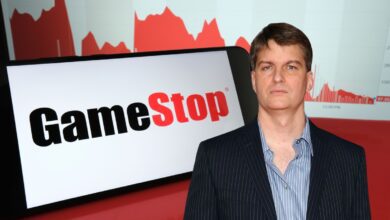 Michael Burry in a pinstripe suit standing in front of a large GameStop logo and red stock chart graphics.