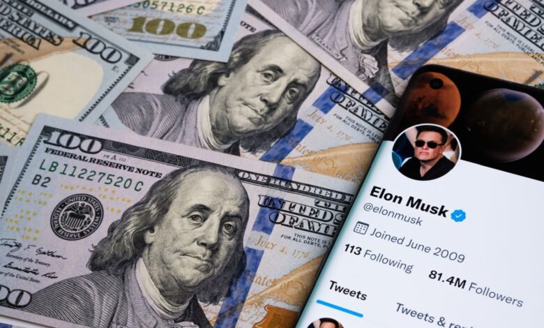Elon Musk Twitter profile on smart phone next to spread out hundred dollar bills.
