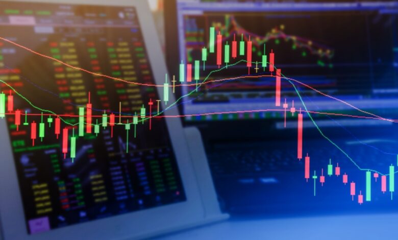 Stock market candlestick chart with trading computer screens in the background.