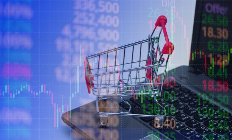 Mini shopping cart on laptop keyboard with stock market charts overlay, symbolizing e-commerce, online retail, and digital stock trading trends.