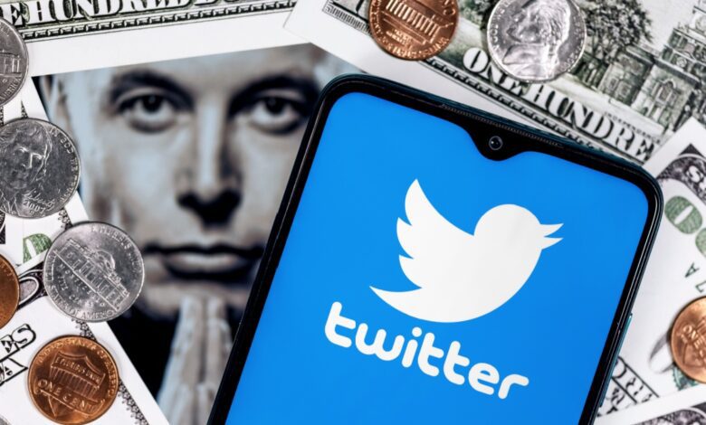 A smartphone displaying the Twitter logo is placed on top of U.S. dollar bills and coins, with a blurred close-up image of Elon Musk's face in the background.