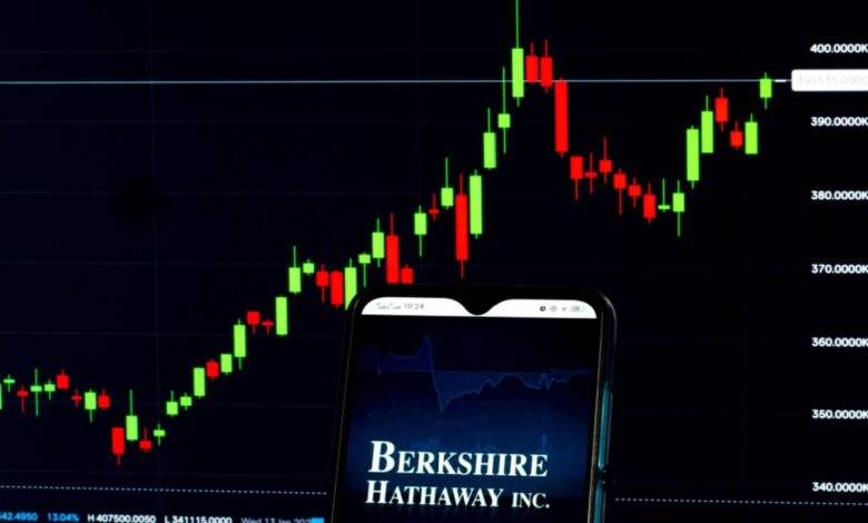 Berkshire Hathaway logo on smartphone with stock chart in background.
