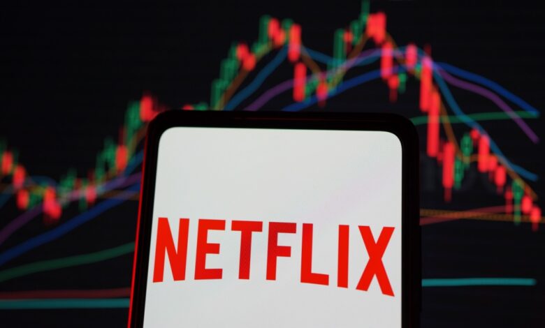 Netflix logo on smartphone screen with declining stock chart in background, illustrating streaming giant’s market performance drop.