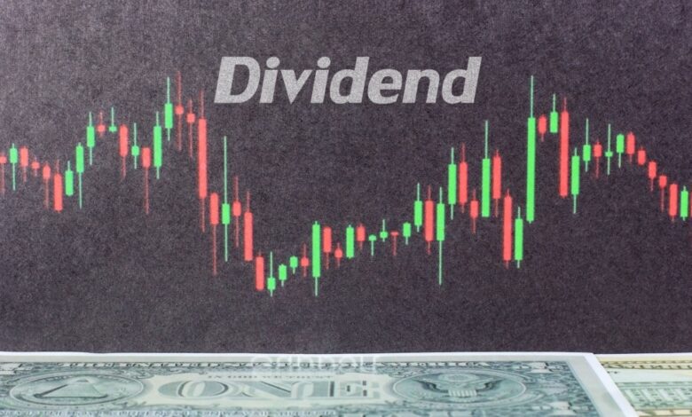 Stock market candlestick chart with the word 'Dividend' in bold above fluctuating red and green candlesticks, symbolizing dividend stock trading and investment analysis, with a U.S. dollar bill partially visible at the bottom, representing financial returns and passive income