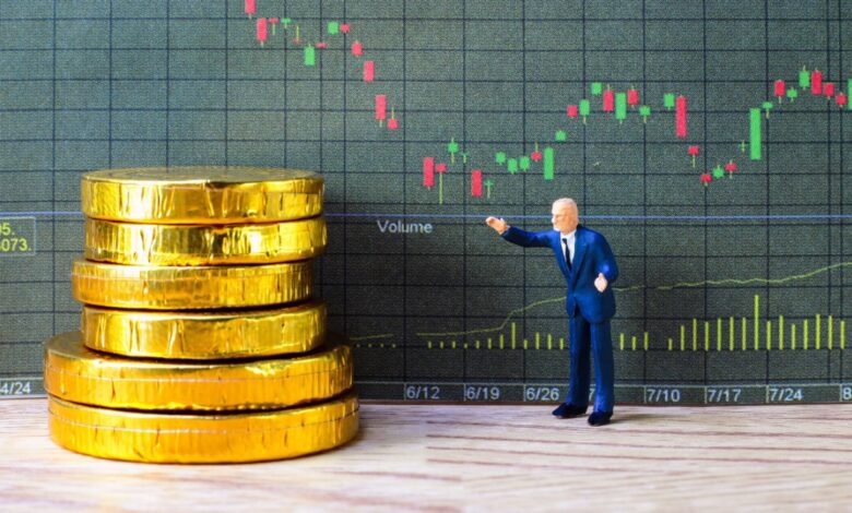 Miniature businessman figure pointing at stacked gold coins in front of a stock market candlestick chart, symbolizing financial investment strategy, economic growth, wealth management, or trading analysis.