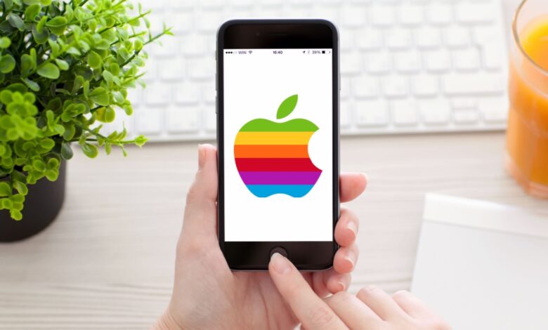 A person's hands holding a iPhone with a rainbow Apple logo on a white screen.