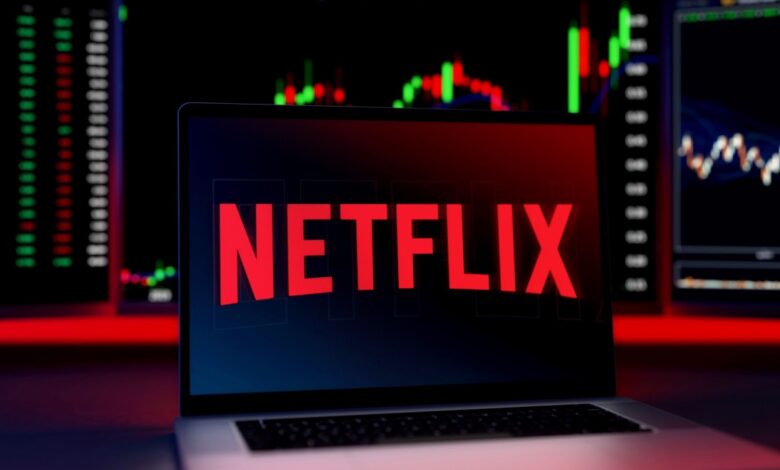 Laptop screen displaying the Netflix logo with stock charts and trading data in the background.