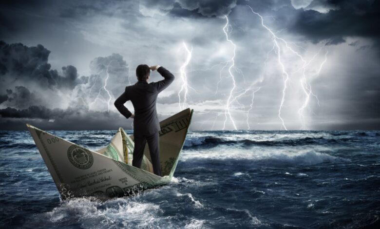 A man in a suit stands on a paper boat made of dollar bills, navigating rough ocean waves while lightning strikes in the stormy sky ahead.