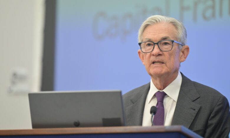 Federal Reserve Chairman Jerome Powell speaking at a podium with a microphone and laptop, in front of a blurred presentation screen, symbolizing economic policy announcement, financial leadership, central banking, and government economic strategy.
