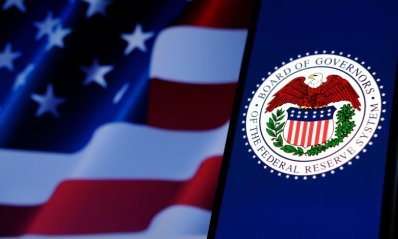 A smartphone displays the seal of the Board of Governors of the Federal Reserve System, with the American flag in the blurred background.