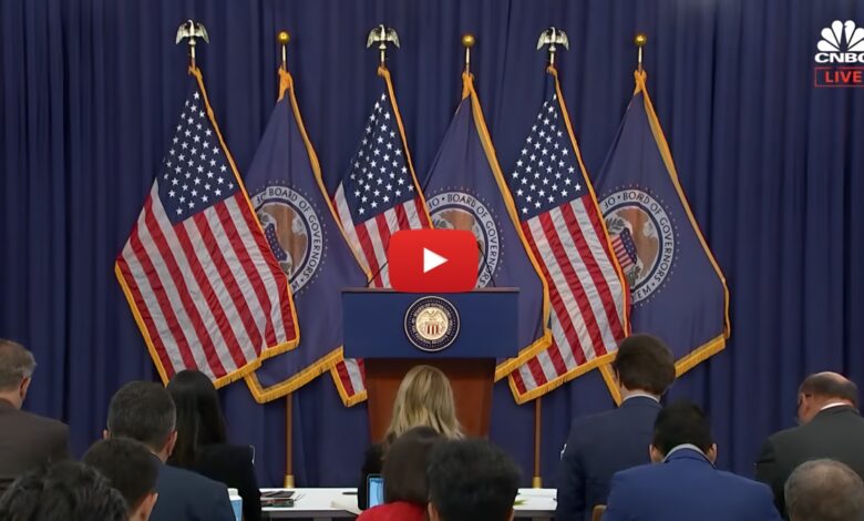YouTube video screenshot of the Federal Reserve press conference setup with podium, U.S. flags, and Federal Reserve seals, streamed live on CNBC with journalists preparing.