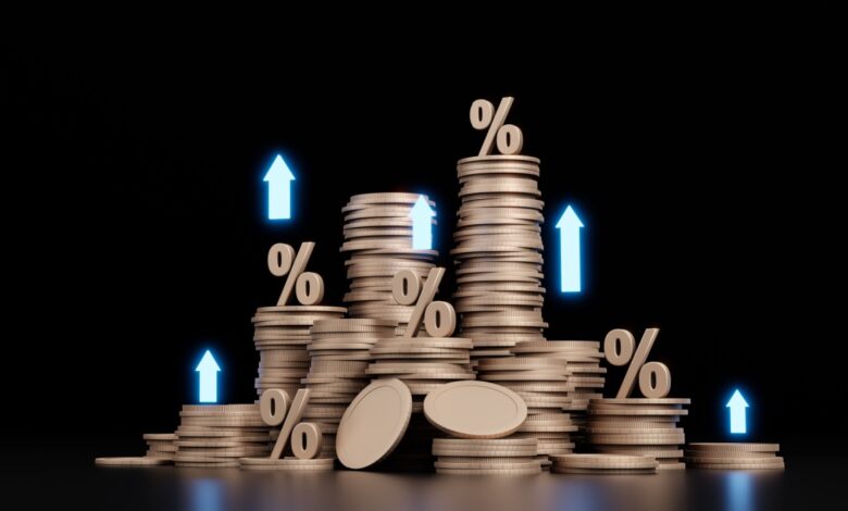 Stacks of coins with percentage signs and upward arrows, symbolizing rising interest rates, inflation, or investment returns in a financial growth concept.