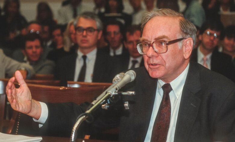 Renowned investor Warren Buffett speaking into a microphone at a formal event, with an audience in the background, symbolizing financial leadership and investment expertise.