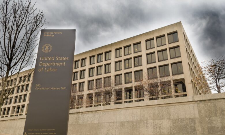 Photo of the Frances Perkins Building taken from ground level looking upward, with a U.S. Department of Labor sign in front and dark storm clouds in the sky.