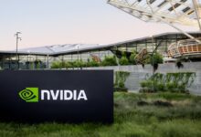 A sign with the NVIDIA logo stands in front of the company’s Voyager building, a modern glass and steel office structure surrounded by greenery.