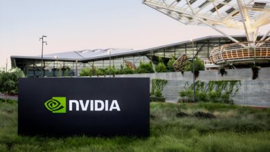 A sign with the NVIDIA logo stands in front of the company’s Voyager building, a modern glass and steel office structure surrounded by greenery.