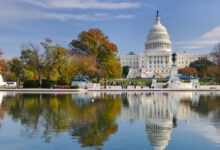 The United States Capitol building in Washington, D.C., viewed from across the reflecting pool on a clear autumn day, with colorful fall trees and visitors walking nearby.