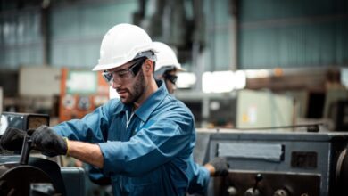 Factory worker in a hard hat and safety glasses operating industrial machinery in a workshop.