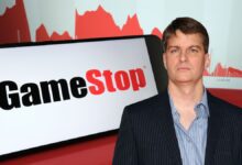 Michael Burry in a pinstripe suit standing in front of a large GameStop logo and red stock chart graphics.