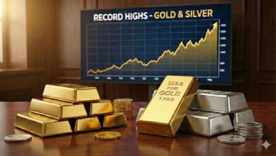 Stacks of gold and silver bars with coins on a wooden table in front of a chart showing record highs in gold and silver prices.