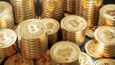 Stacks of shiny gold-colored coins featuring the Bitcoin symbol, representing cryptocurrency wealth or investment.