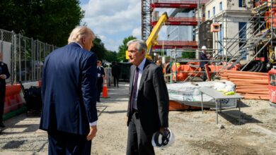 President Trump and Federal Reserve Chair Jerome Powell talk at the Fed Building construction site with scaffolding, equipment, and workers in the background.
